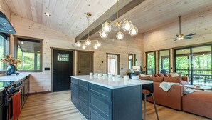 Een ruime keuken met een centraal kookeiland, houten vloeren en een moderne hanglamp.