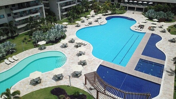 A large, multi-pool resort with a central swimming area, surrounded by lounge chairs and umbrellas. - CoHost Flat BeachClass EcoLife 104G (IPOJUCA)