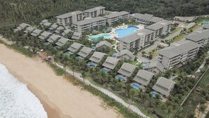 An aerial view of a resort with multiple buildings, a central swimming pool, and a beachside location. - CoHost Flat BeachClass EcoLife 104G (IPOJUCA)