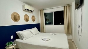 A hotel room with a bed, a TV mounted on the wall, an air conditioning unit, and a window with curtains. - CoHost Flat Porto Plaza 409 (IPOJUCA)