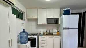A kitchen with white cabinets, a stove, a microwave, a refrigerator, and a water dispenser. - CoHost Flat Porto Plaza 409 (IPOJUCA)