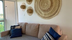 A living room with a beige sofa, two pillows, and a large woven wall hanging. - CoHost Flat Porto Plaza 409 (IPOJUCA)