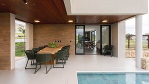 Un área de comedor exterior moderna con piscina, techo de madera y puertas de cristal que dan a un patio.