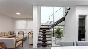 Una sala de estar moderna con una escalera, un sofá, una mesa de centro y vistas amplias a través de grandes ventanales.