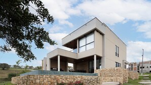 Una casa moderna de dos pisos con cimientos de piedra, ventanas amplias y un espacio exterior cubierto.