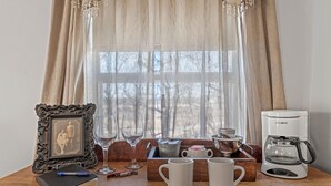 A wooden table with a framed picture, a notebook, a pen, two wine glasses, a mug, a coffee maker, and a kettle. - Romance Suite at B&B with full breakfast & mimosas! (Fredericksburg)
