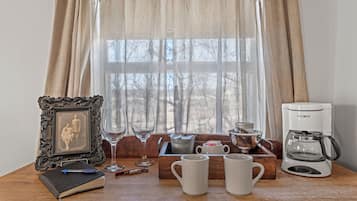 A wooden table with a framed picture, a notebook, a pen, two wine glasses, a mug, a coffee maker, and a kettle.