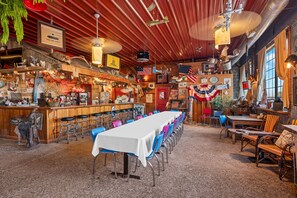 Un restaurante con una larga mesa, zona de bar y diversas decoraciones, incluyendo banderas y un reloj.