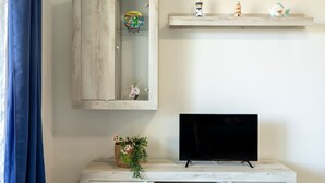 A living room with a TV on a wooden stand, a cabinet with a decorative plate, and a shelf with figurines. - Sardinia Re - Armonia 9 (Castelsardo)