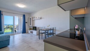 A modern kitchen with a dining area, a TV, and a balcony with a view. - Sardinia Re - Armonia 9 (Castelsardo)