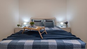 A neatly made bed with a checkered bedspread, two bedside lamps, a small table with a tray, and a potted plant on the nightstand. - Sardinia Re - Armonia 9 (Castelsardo)