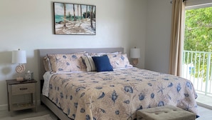 Une chambre à coucher comprenant un lit, un ventilateur de plafond, une table de chevet avec une lampe, une commode et une fenêtre avec des rideaux.