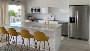 Une cuisine moderne avec des meubles blancs, un réfrigérateur en acier inoxydable, un four à micro-ondes et un grand îlot central doté de tabourets de bar.