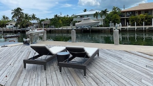 Une terrasse en bois avec des chaises longues et une vue sur une marina où l’on peut admirer des bateaux et des maisons.
