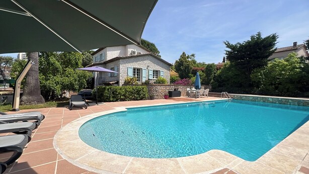 Ein Schwimmbecken mit Steinbord, Liegestühlen und einer Sonnenterrasse mit Sonnenschirmen.