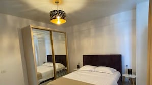 A bedroom with a bed, a wardrobe, a nightstand, and a hanging light fixture. - Apartament Mamaia Nord (Năvodari)