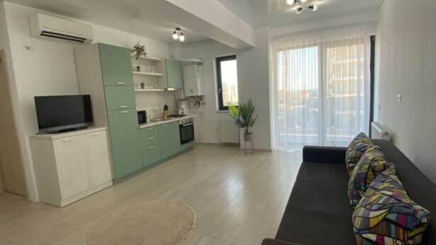A spacious living area with a sofa, a television, and a kitchen in the background. - Apartament Mamaia Nord (Năvodari)