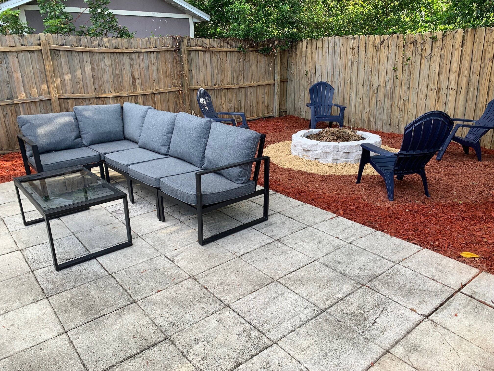 A patio with a sectional sofa, two chairs, and a small fire pit.