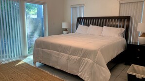 Une chambre avec un grand lit, deux tables de chevet, une commode, une fenêtre avec des stores et une vue sur la verdure.