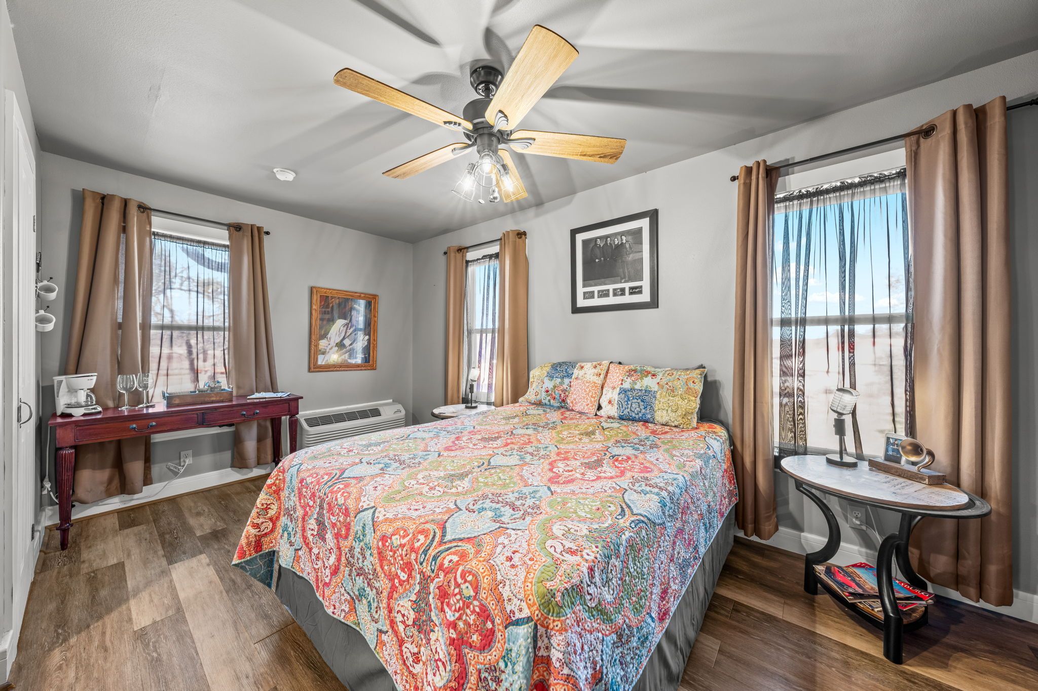 A bedroom with a bed, a desk, a chair, a ceiling fan, and a window with curtains.