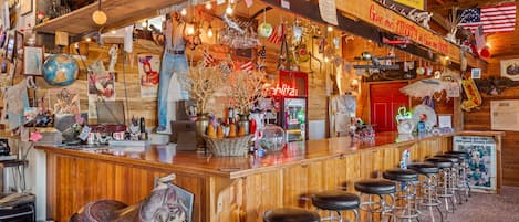 A bar area with wooden bar counter, stools, and various decorations including flags and a neon sign.