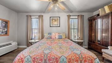 A bedroom with a large bed, a ceiling fan, a framed picture on the wall, and a window with curtains.