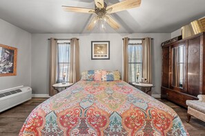 A bedroom with a large bed, a ceiling fan, a framed picture on the wall, and a window with curtains. - Texas Music Suite B&B in Luckenbach, TX! Hot breakfast & Mimosas! (Fredericksburg)