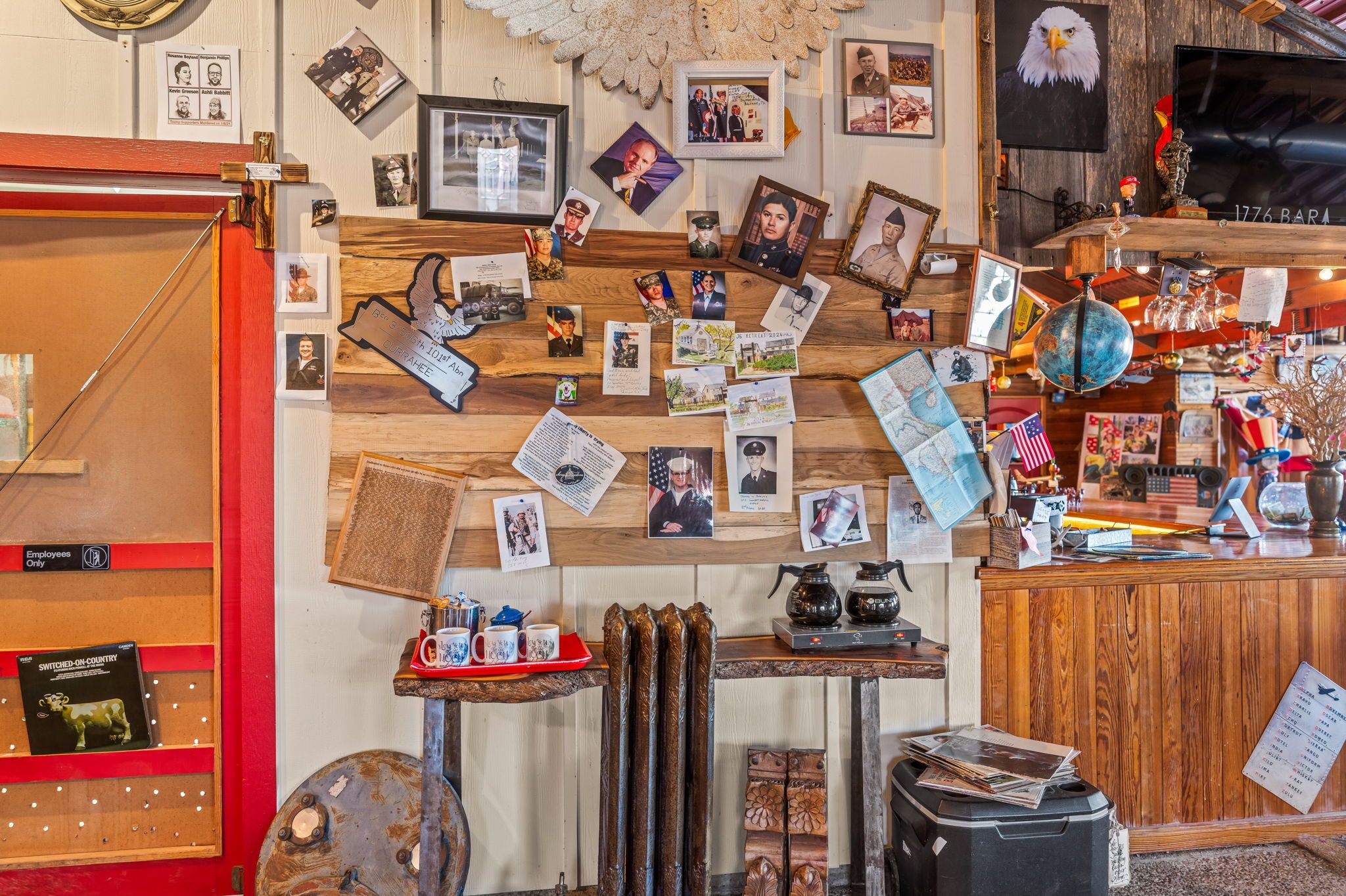 Ein Zimmer mit einer Holzwand, die mit verschiedenen Fotos und Erinnerungsstücken dekoriert ist, einem Holztresen und einem Bücherregal mit rotem Rahmen.
