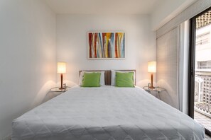 A hotel room with a bed, two bedside lamps, a colorful abstract painting, and a window with blinds. - 801 (Rio de Janeiro)