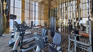 Ein modernes Fitnessstudio mit unterschiedlichen Trainingsgeräten, großen Fenstern und einem gemusterten Teppich.