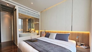 Ein modernes Hotelzimmer mit einem großen Bett, einem Nachttisch mit Lampe und einem durchgegangene Tür einsehbaren Badezimmer.