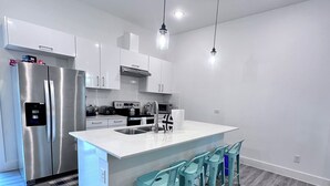 A modern kitchen with a central island, stainless steel appliances, and teal bar stools. - 3 comfy king beds, hot tub, EV, cozy (Fort Worth)