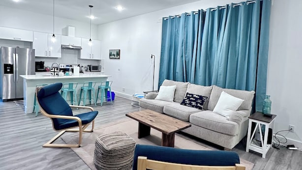 A modern living room with a sofa, two armchairs, a coffee table, and a kitchen in the background. - 3 comfy king beds, hot tub, EV, cozy (Fort Worth)