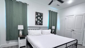 A neatly arranged bedroom with a bed, two bedside tables with lamps, a ceiling fan, and a door. - 3 comfy king beds, hot tub, EV, cozy (Fort Worth)
