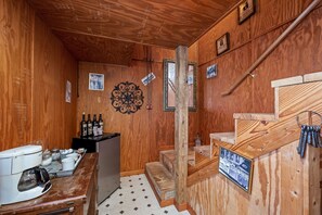 Un interior de madera con una máquina de café, un refrigerador pequeño y una escalera de madera.