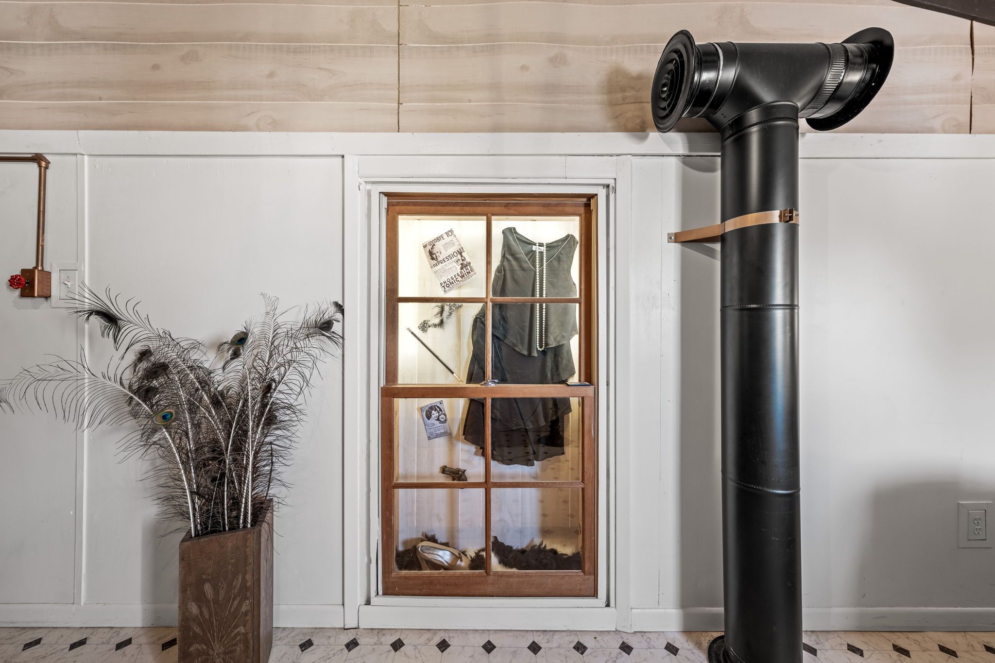 A room with a wooden door, a peacock feather decoration, and a black pipe.