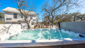 Un bain à remous avec jets d’eau, entouré d’arbres, avec une maison en arrière-plan.