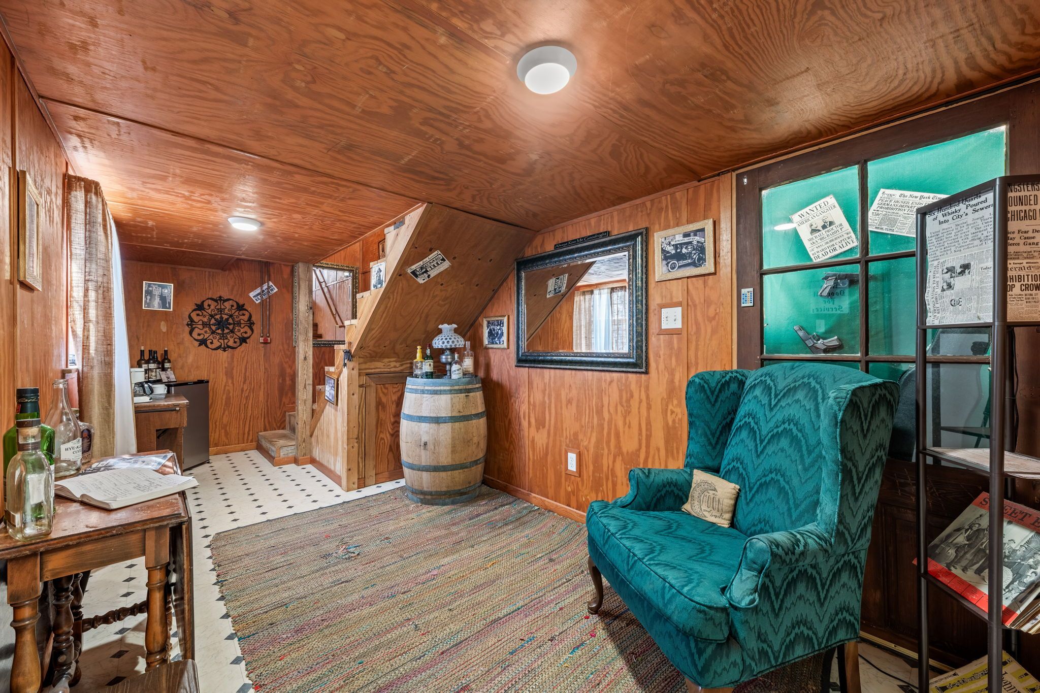 A wooden interior with a green armchair, a wooden barrel, and a mirror on the wall.