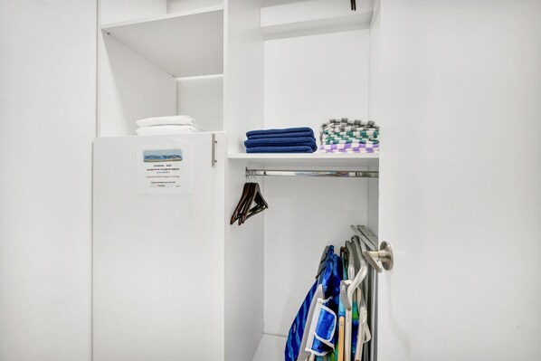 A white room with a door, a shelf with folded towels, and a rack with cleaning supplies.