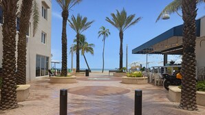 A courtyard with palm trees, a tiled floor, and a view of the beach.