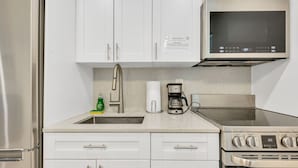 Una cocina moderna con armarios blancos, electrodomésticos de acero inoxidable, microondas integrado y cafetera.