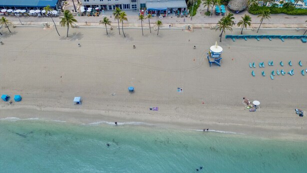 Vista aérea de una playa con aguas turquesas cristalinas, palmeras y sombrillas.