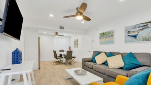 A modern living room with a grey sofa, yellow armchair, white coffee table, and a TV on a white stand. - Cozy two bedroom, feet from the beach (Hollywood)