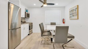 A compact kitchen with a refrigerator, stove, microwave, and a dining area with chairs and a table. - Cozy two bedroom, feet from the beach (Hollywood)