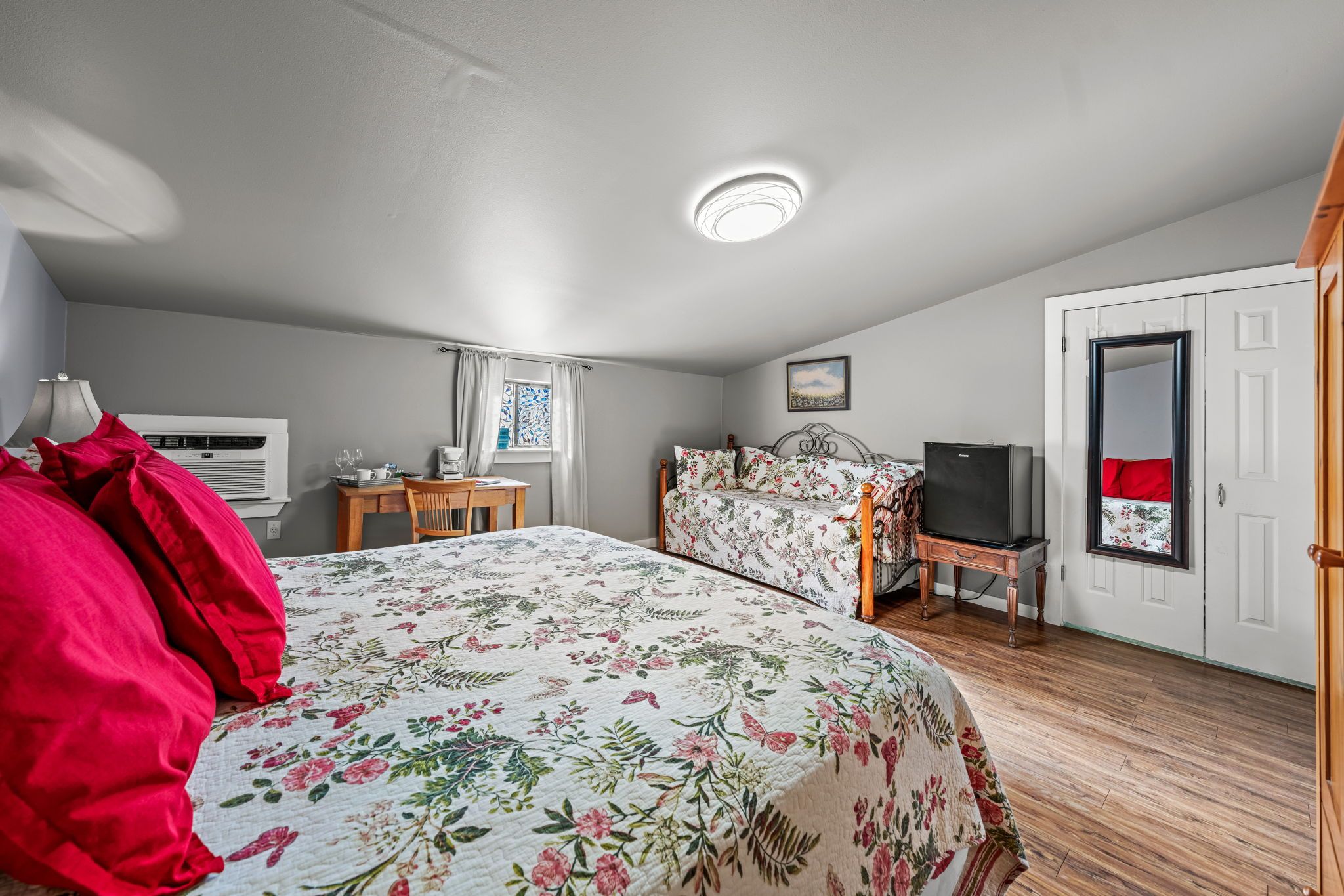 A bedroom with a bed, a desk, a chair, a wardrobe, and a mirror.