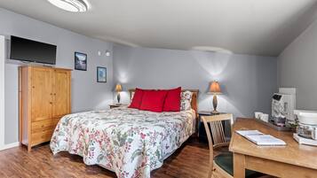 Una camera da letto con un letto, un'armadio in legno, una scrivania con una sedia, una macchina da caffè e un televisore appeso al muro.