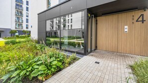 Ein moderner Hauseingang mit Glastür, einer Holztür mit der Nummer 4 und einem gefliesten Weg, der zu einem Garten führt.