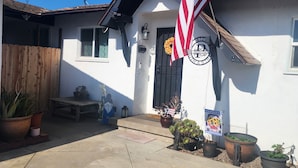 A white building with a black door, a wooden fence, and several potted plants. - Charming 3-bedroom house in fabulous Oxnard with WiFi (Oxnard)
