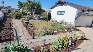 A residential garden with a paved walkway, various plants, and a garage. - Charming 3-bedroom house in fabulous Oxnard with WiFi (Oxnard)