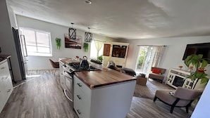 A modern kitchen with a central island, wooden flooring, and a dining area with a sofa and table. - Charming 3-bedroom house in fabulous Oxnard with WiFi (Oxnard)